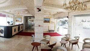 A hotel lobby with a reception desk, seating area, chandeliers, and a large window with text. - Ikram el Dhayf (Algiers)