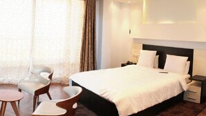 A hotel room with a large bed, two chairs, a small table, and a nightstand with a lamp. - Ikram el Dhayf (Algiers)