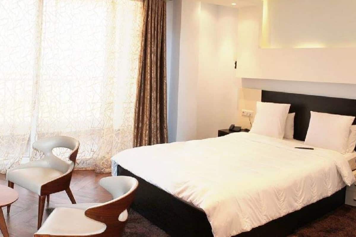 A hotel room with a bed, two chairs, a small table, and a nightstand with a lamp.