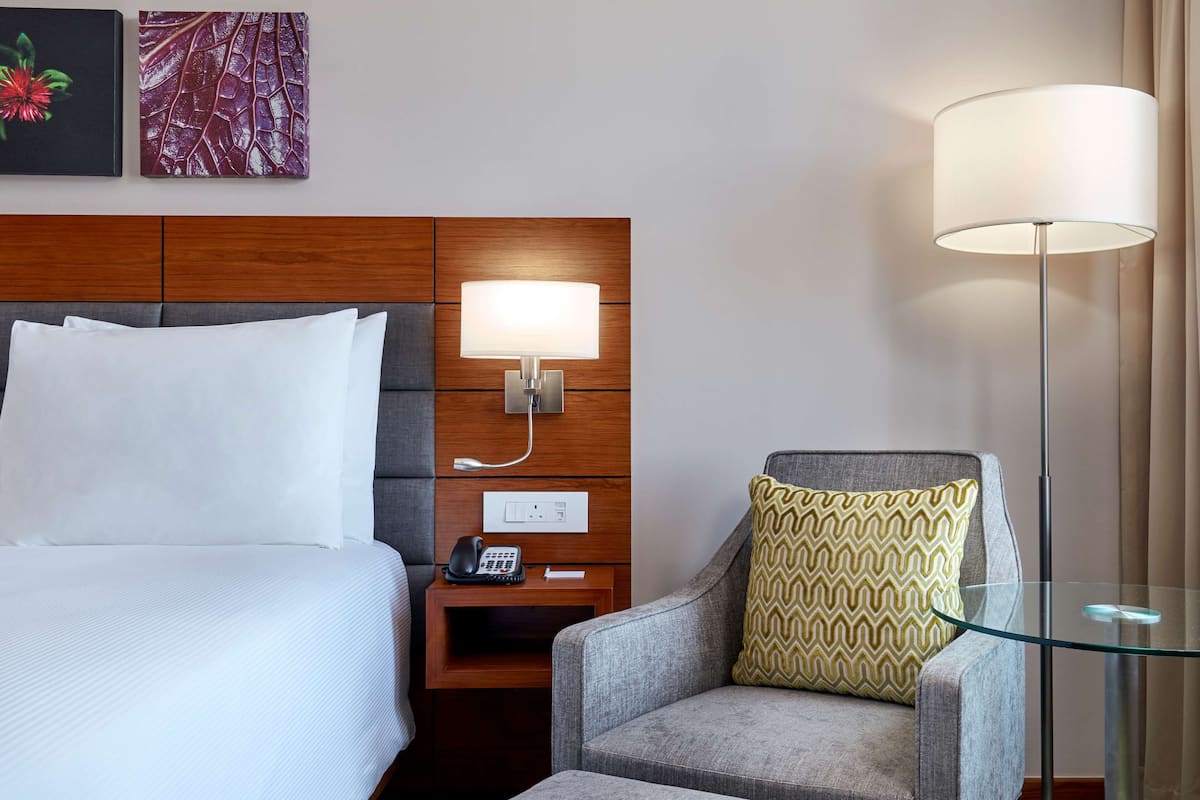 Una habitación de hotel con una cama, una mesita de noche con un teléfono, una lámpara y una silla con un cojín estampado.
