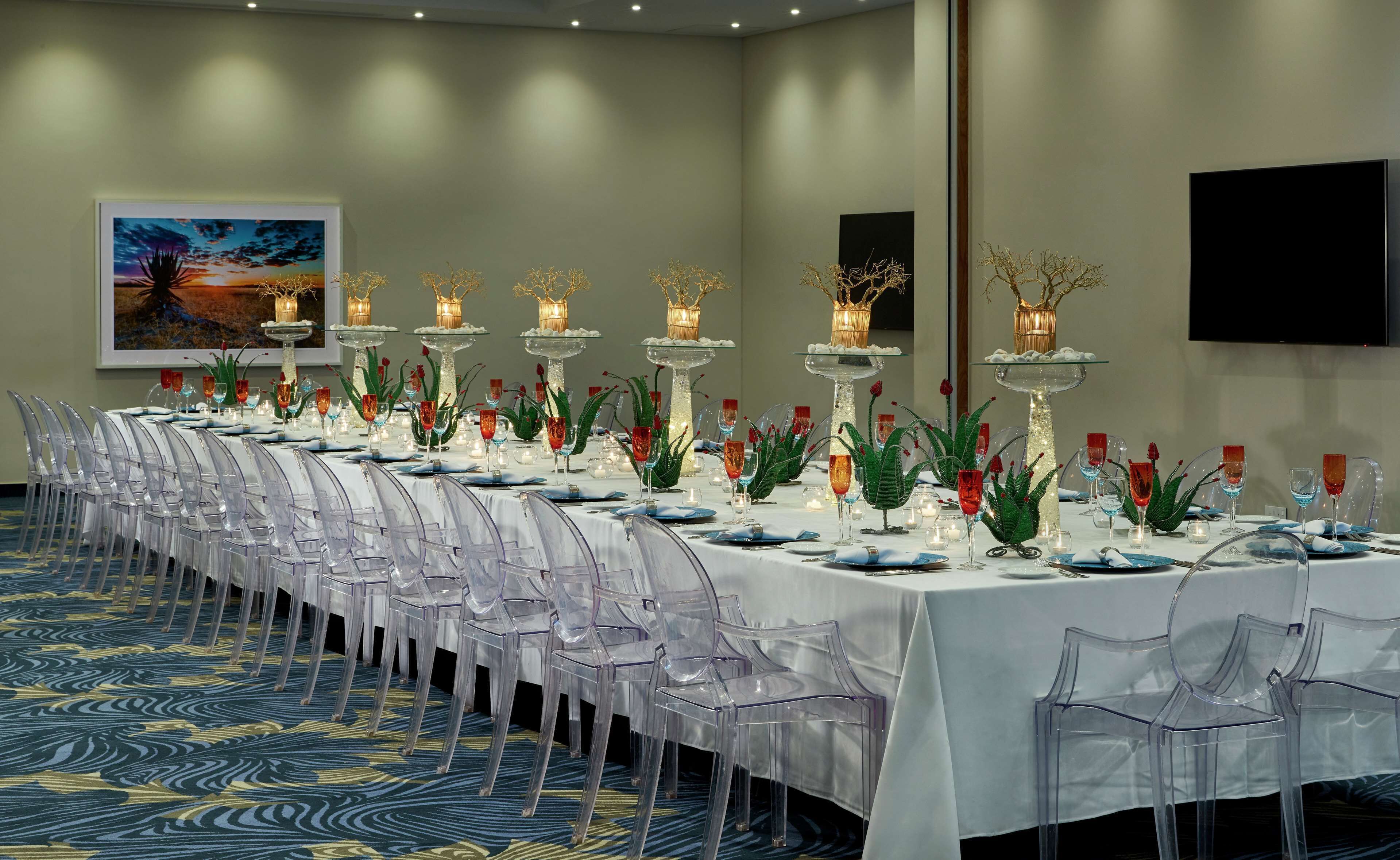 Una larga mesa de comedor dispuesta con sillas transparentes, velas y jarrones decorativos.