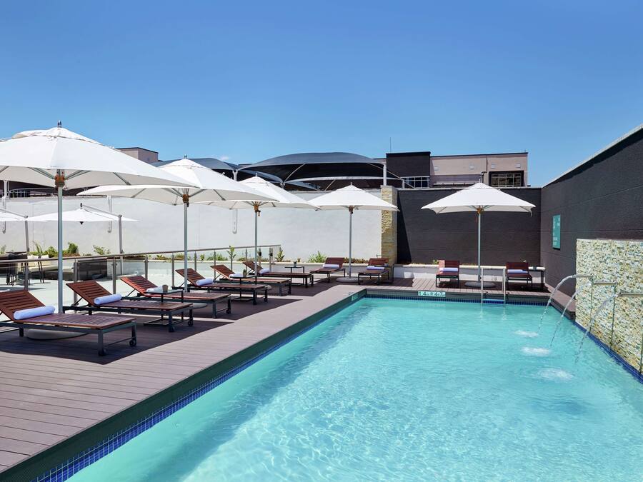 A pool area with sun loungers and umbrellas, a clear blue pool, and a modern building in the background.