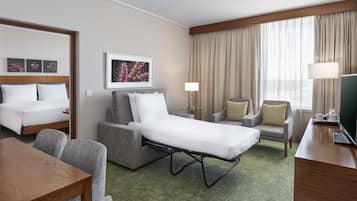 A hotel room with a bed, a sofa, a desk, and a TV. There are two chairs, a lamp, and a picture on the wall.