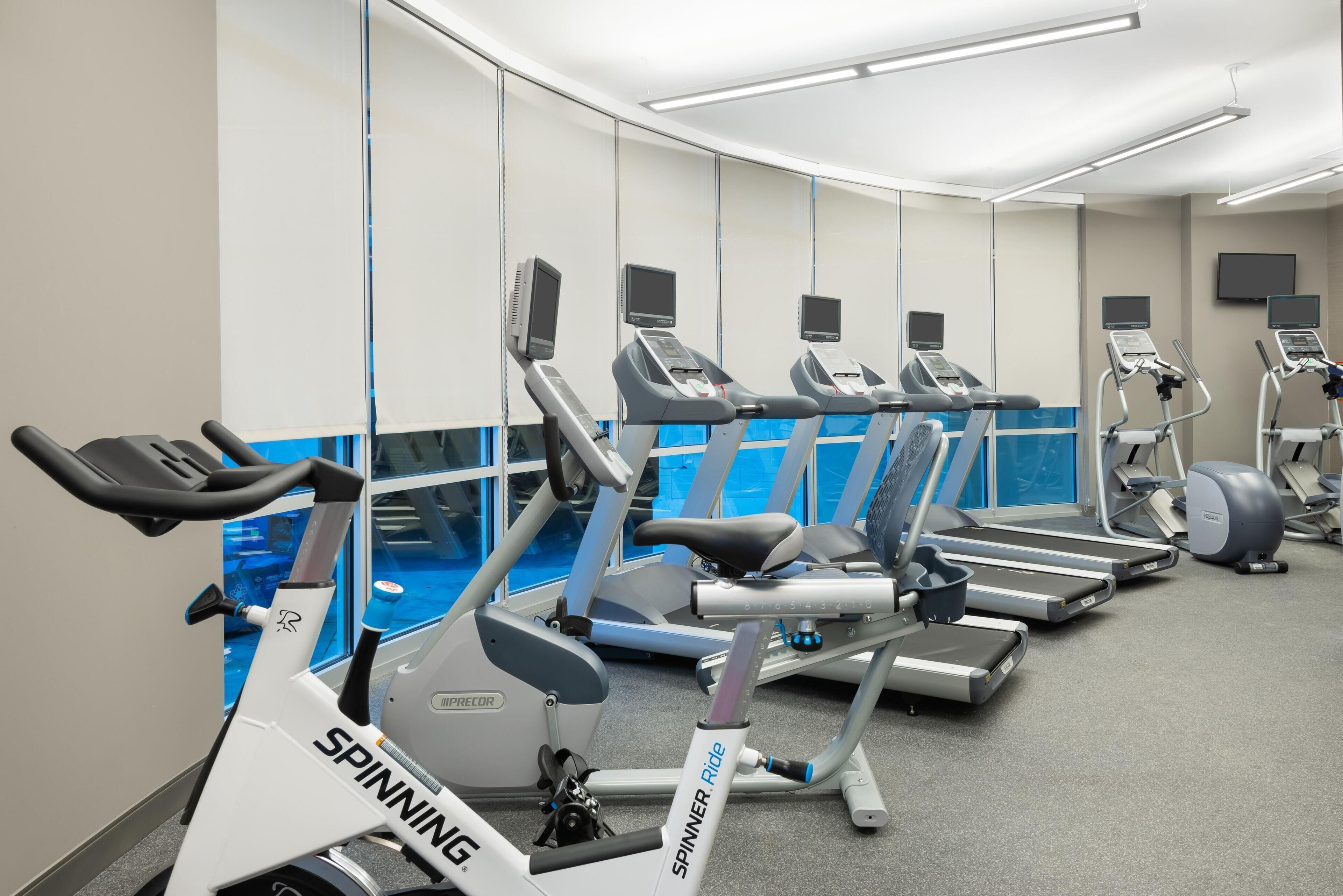 Een sportschool met diverse cardioapparaten, waaronder loopbanden en hometrainers, en een grote spiegelwand.