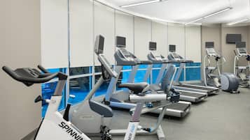 A gym with multiple cardio machines, including treadmills and stationary bikes, and a large mirror wall.