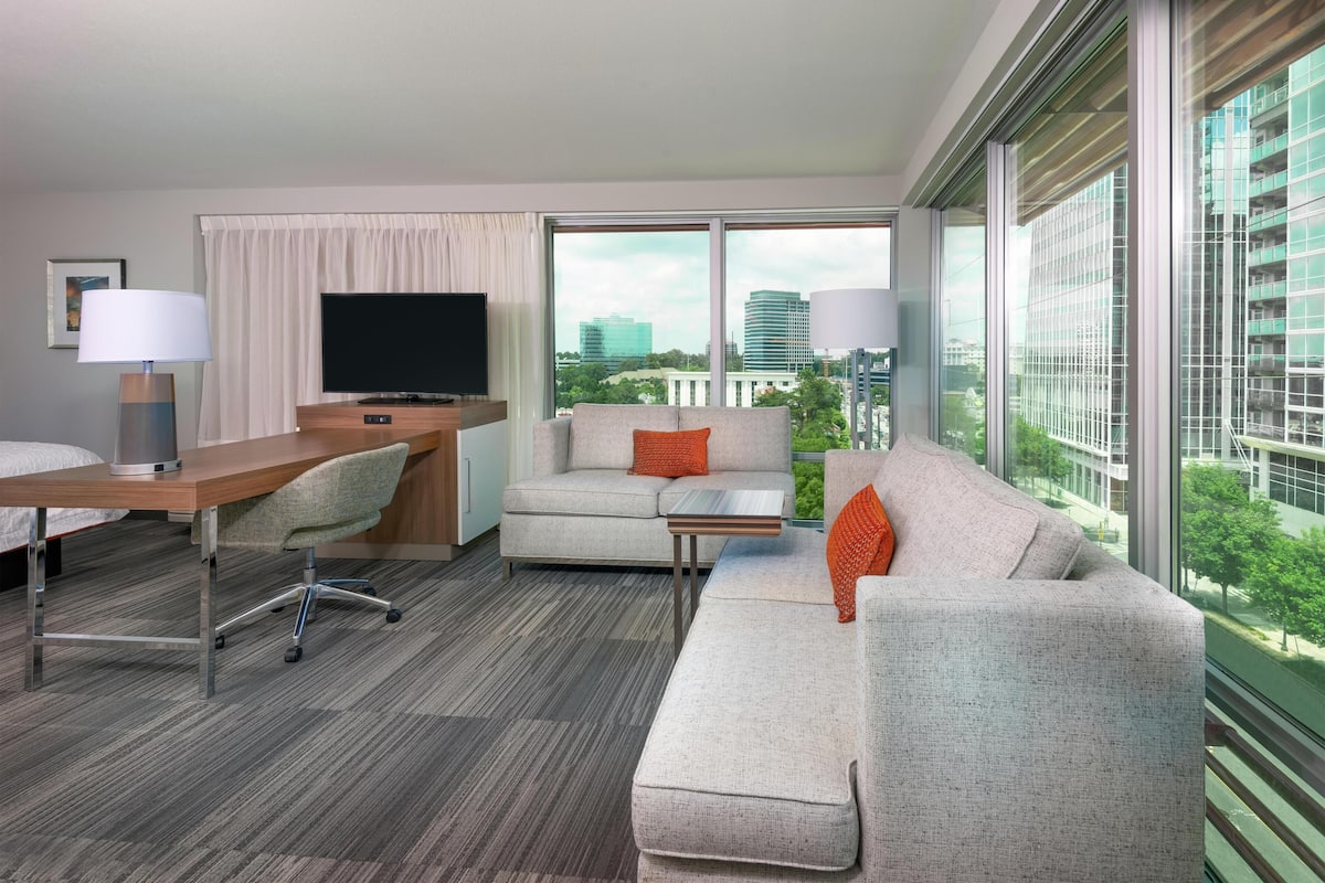 Una habitación de hotel moderna con un amplio ventanal, un televisor de pantalla plana, un escritorio, un sofá y una mesa de centro.