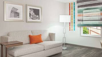 A modern living room with a grey sofa, a small wooden side table, a floor lamp, and two framed pictures on the wall.