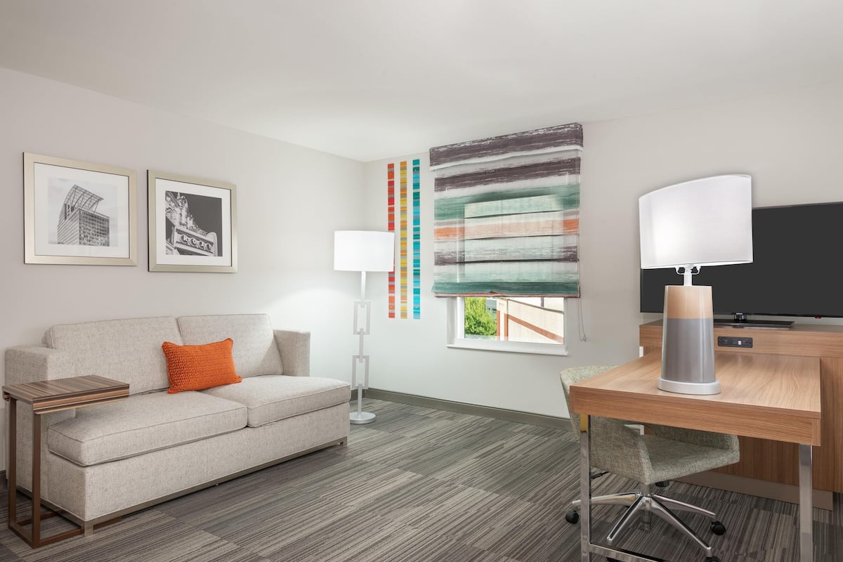 Una habitación de hotel moderna con un sofá, un escritorio, una lámpara de pie y un cuadro abstracto grande en la pared.