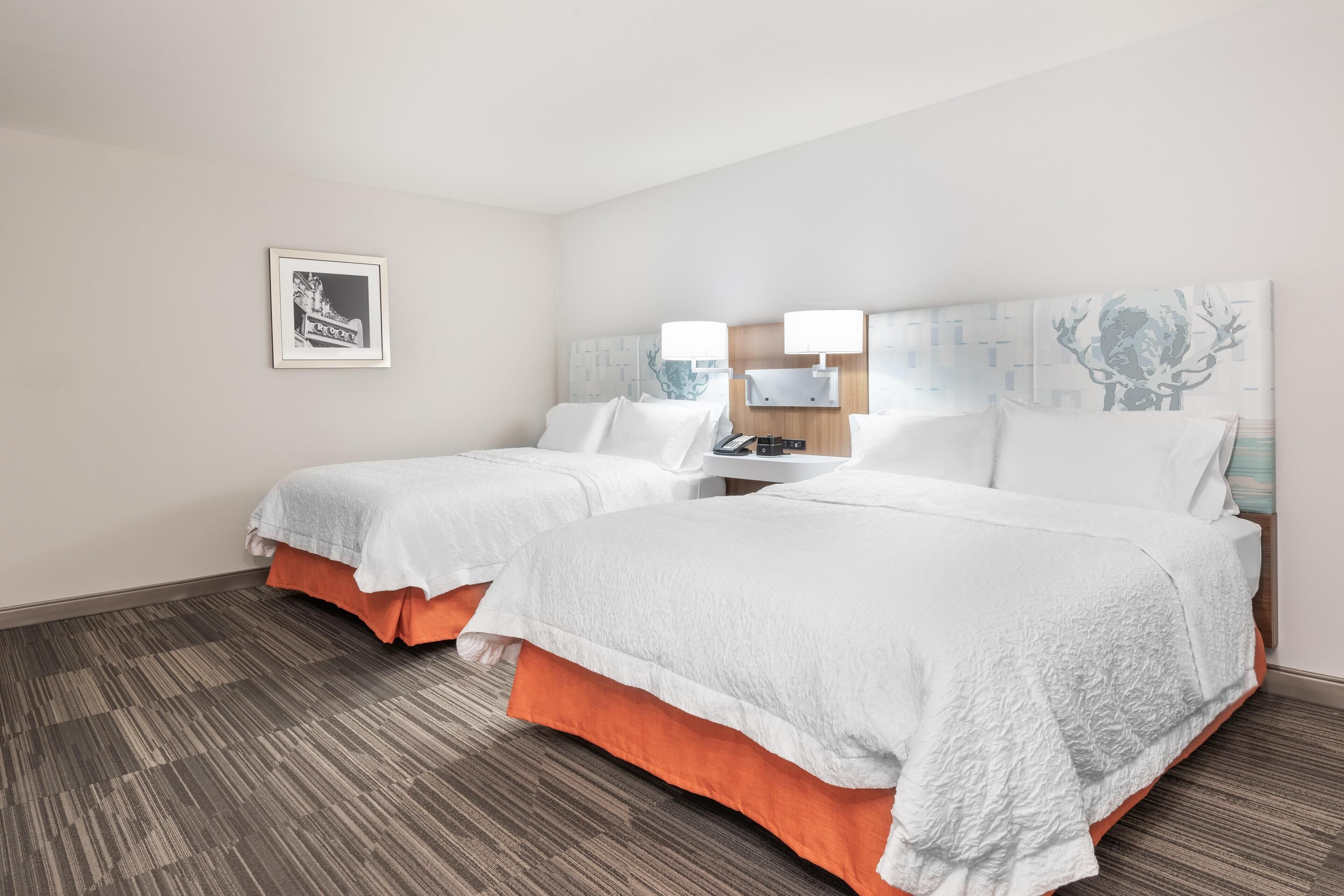 A hotel room with two beds, a nightstand, a framed picture, and a patterned carpet.