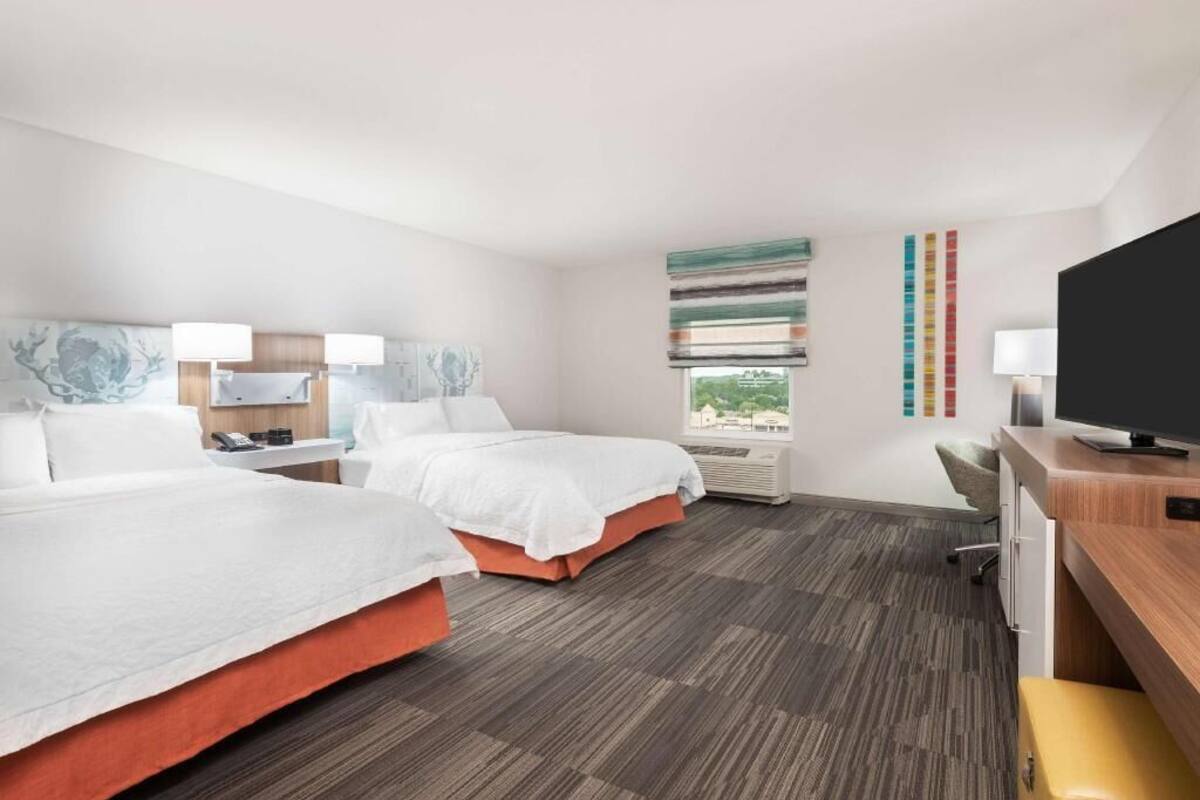 Habitación de hotel con dos camas, un escritorio, una televisión y ventana con vistas.