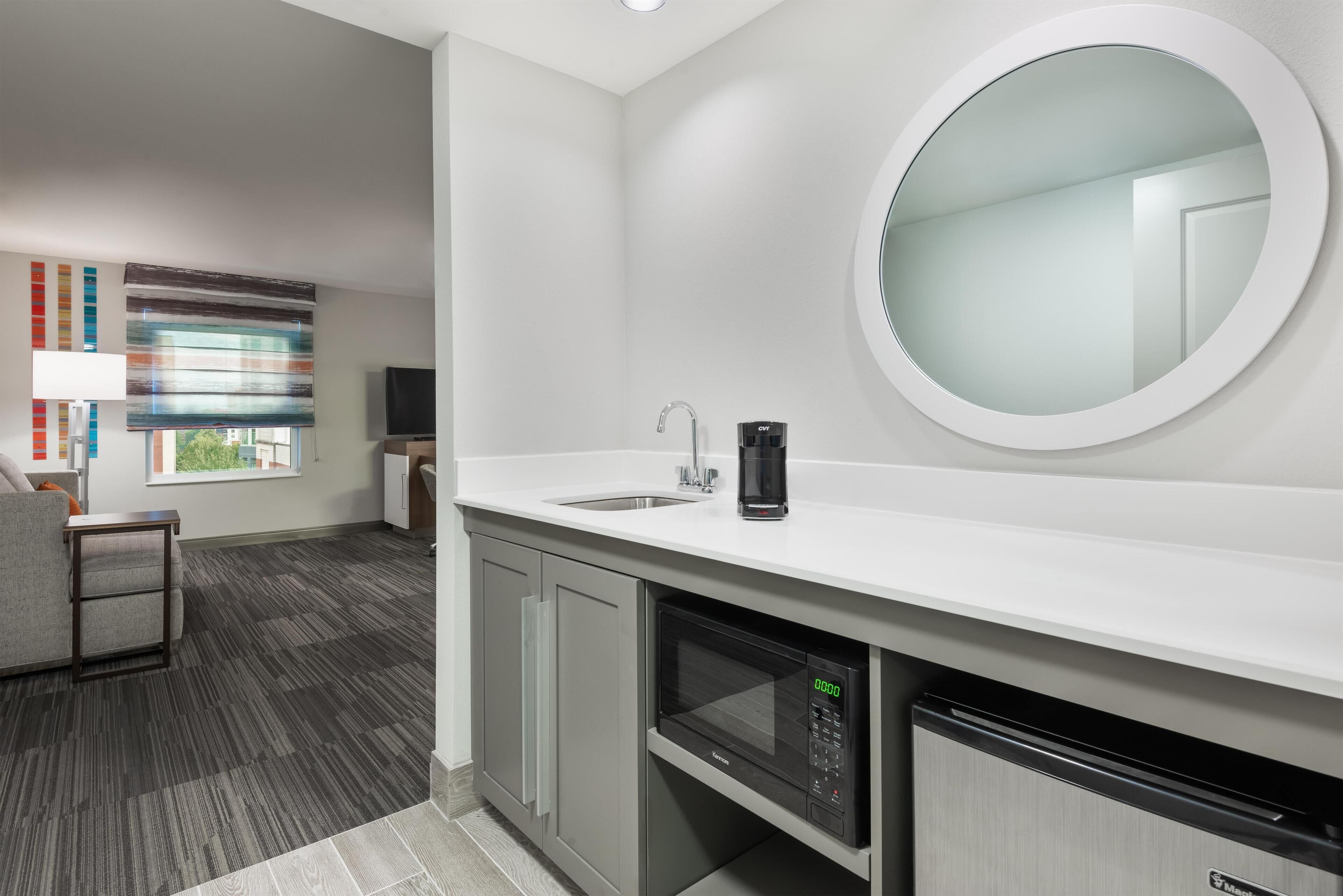 A modern bathroom with a large mirror, a sink, a coffee maker, and a dishwasher.