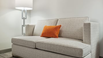 A grey sofa with a textured fabric, a single orange cushion, and a modern floor lamp with a white shade.