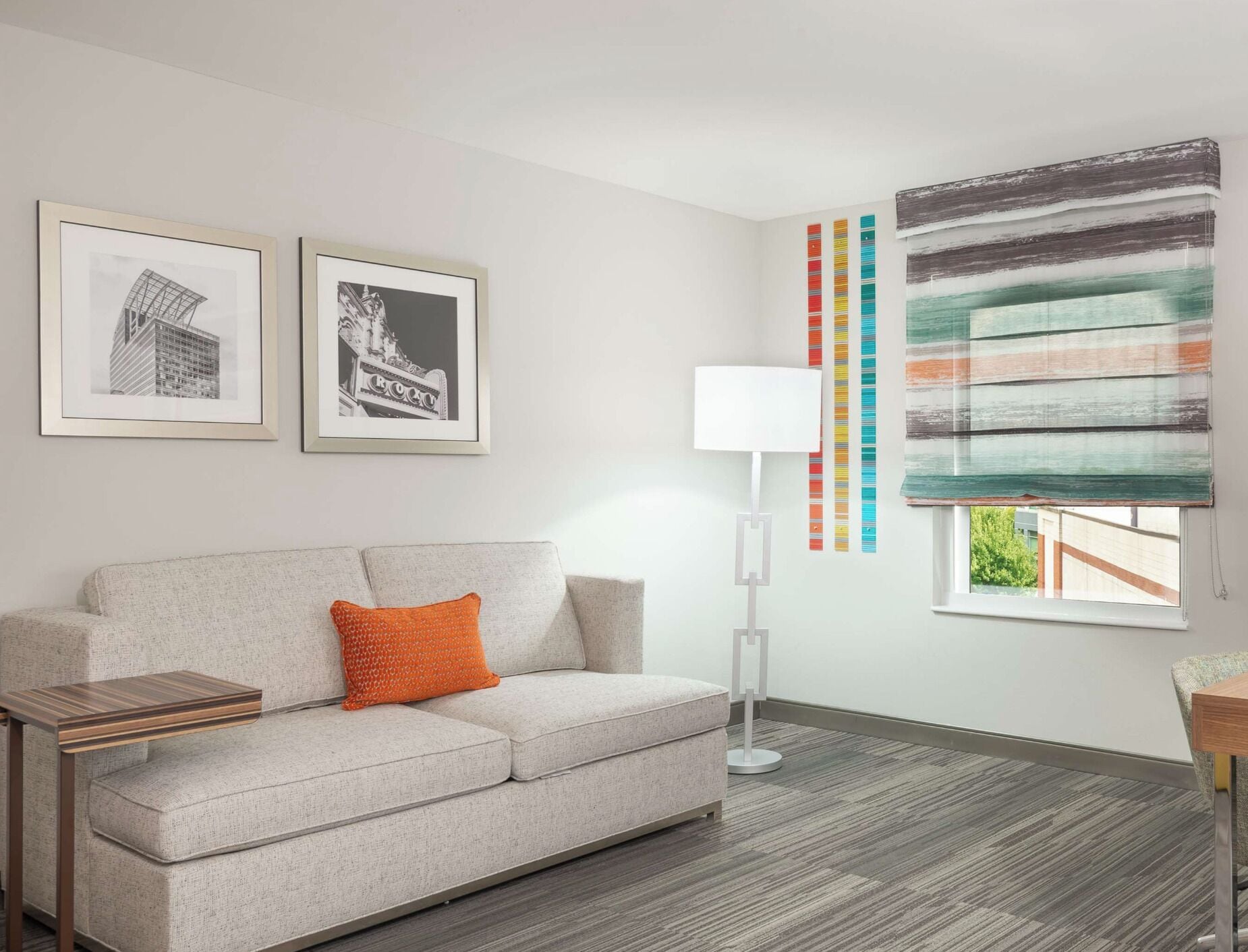 A modern living room with a sofa, a side table, a floor lamp, and two framed pictures on the wall.