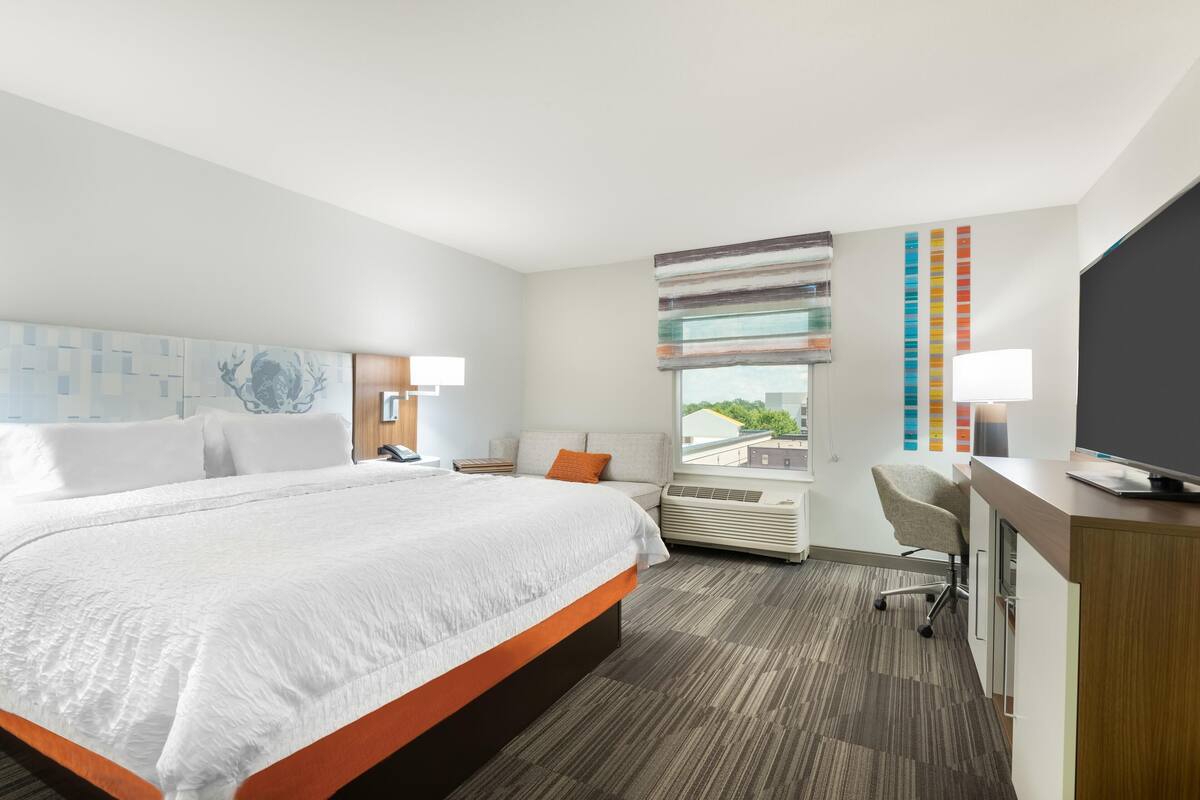 Habitación de hotel con una cama grande, un escritorio, una silla y un televisor.