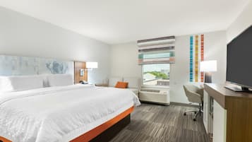 A hotel room with a large bed, a desk, a chair, and a TV.