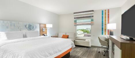 A hotel room with a large bed, a desk, a chair, and a TV.