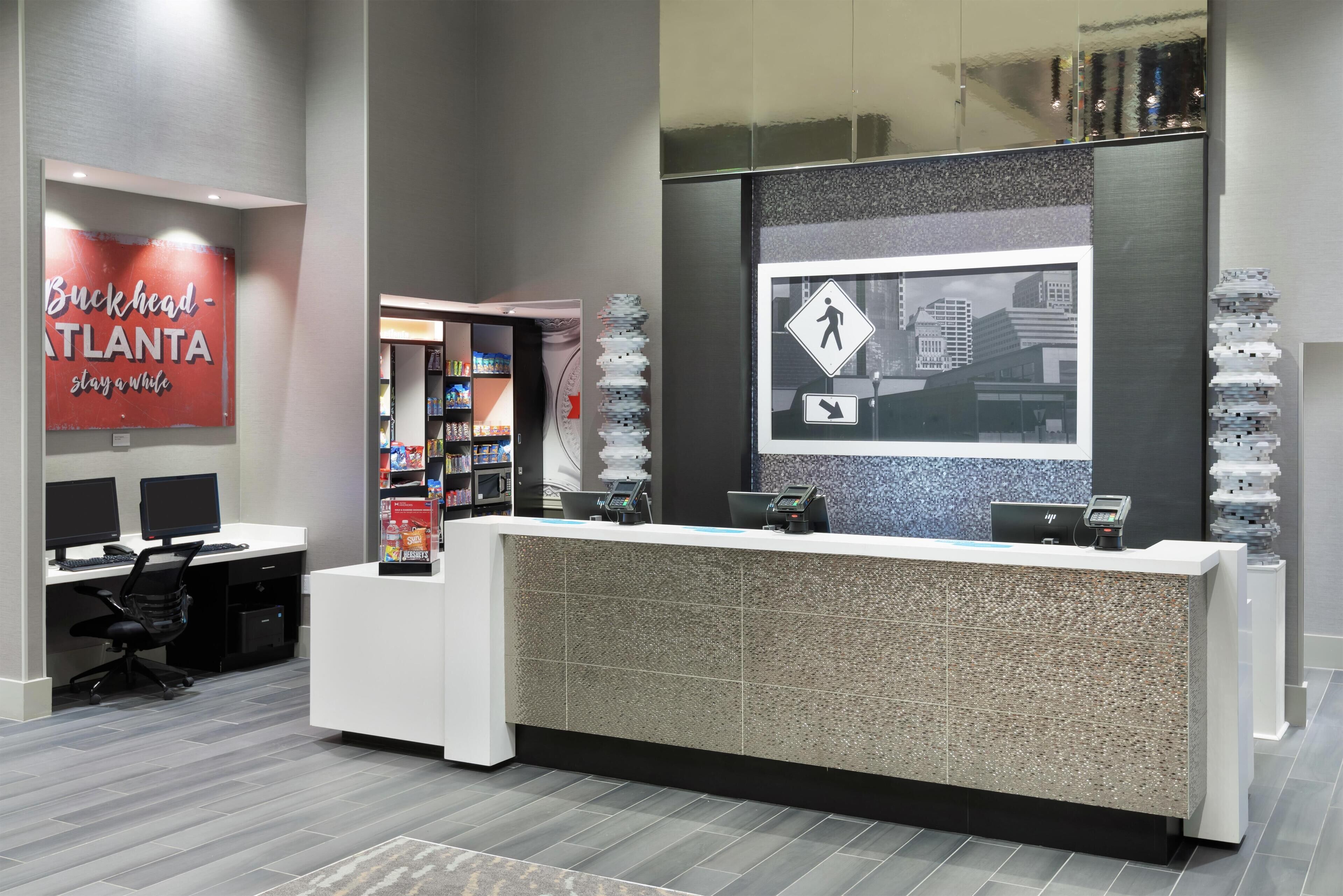 A modern reception desk with a cityscape mural, a sign for Buckhead Atlanta, and a computer setup with two monitors.