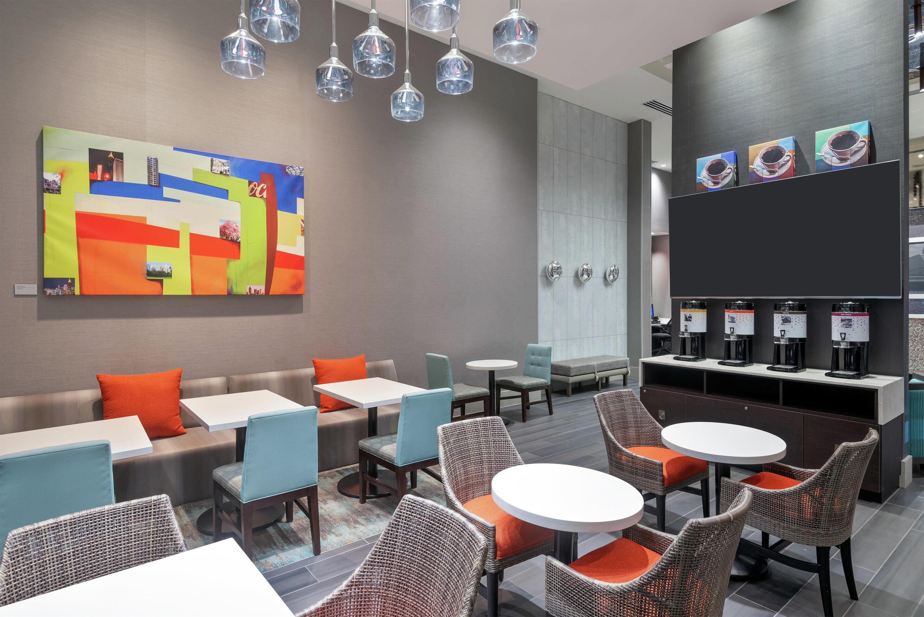 A modern lounge area with seating arrangements, a coffee station, and a large abstract painting on the wall.