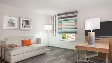 A modern hotel room with a sofa, a desk, a lamp, and a large abstract painting.