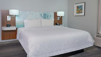 A hotel room with a large bed, two bedside tables with lamps, a wall-mounted phone, a framed picture, and a carpeted floor.