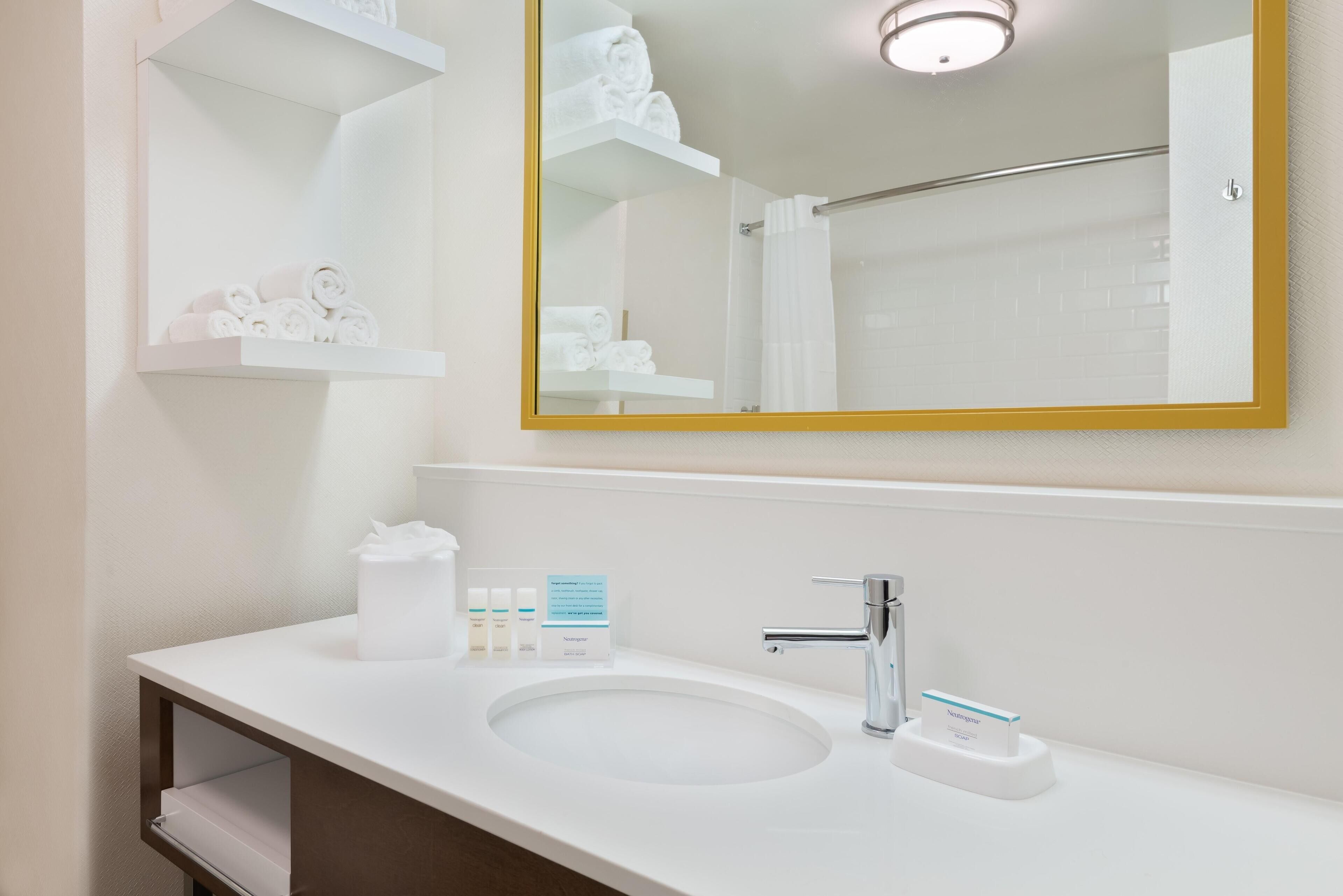 Un baño moderno con un lavamanos blanco, un espejo grande y estantes con toallas.