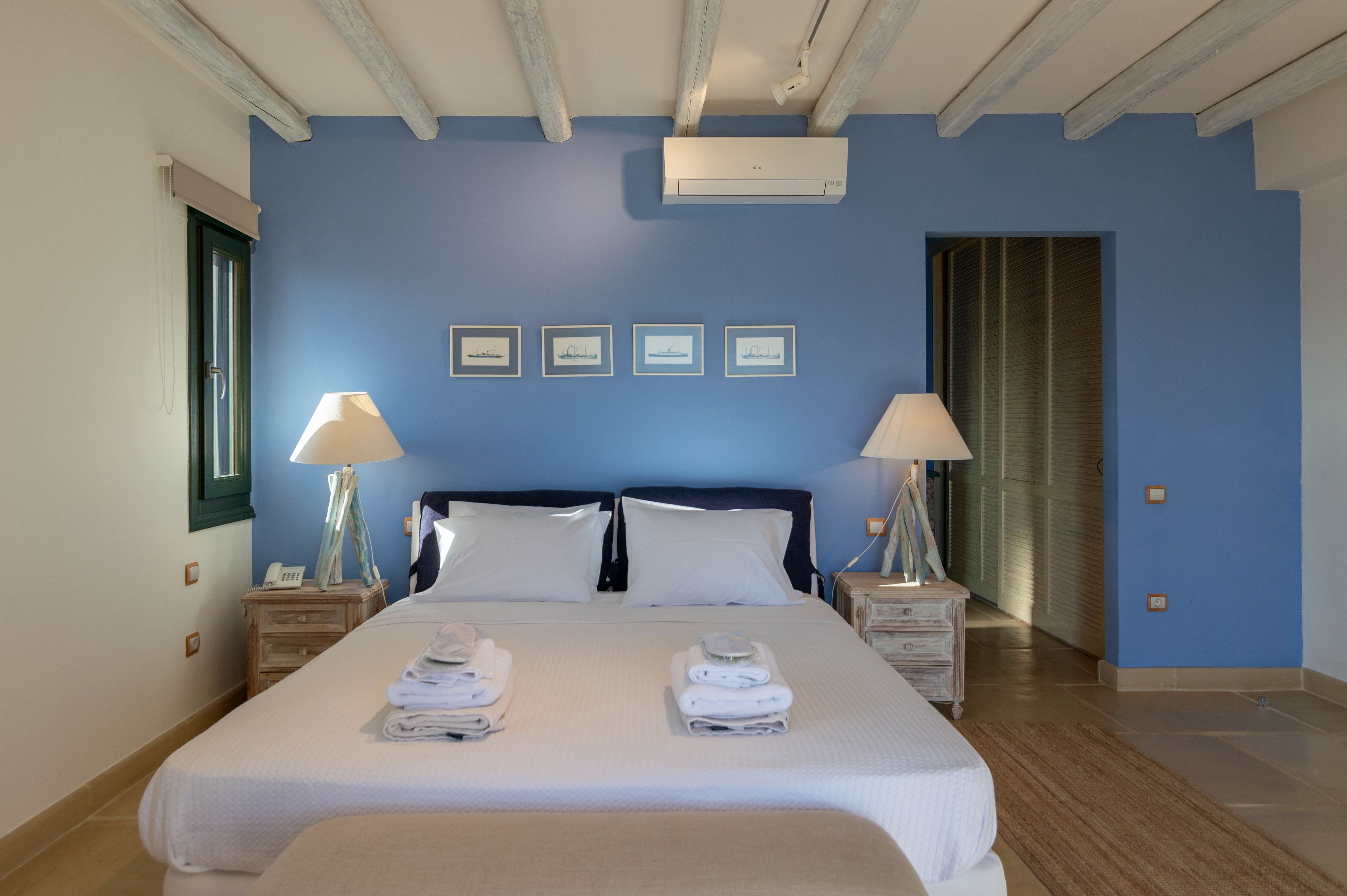 A hotel room with a large bed, two bedside tables, two lamps, a window with a curtain, and a door with a shutter.