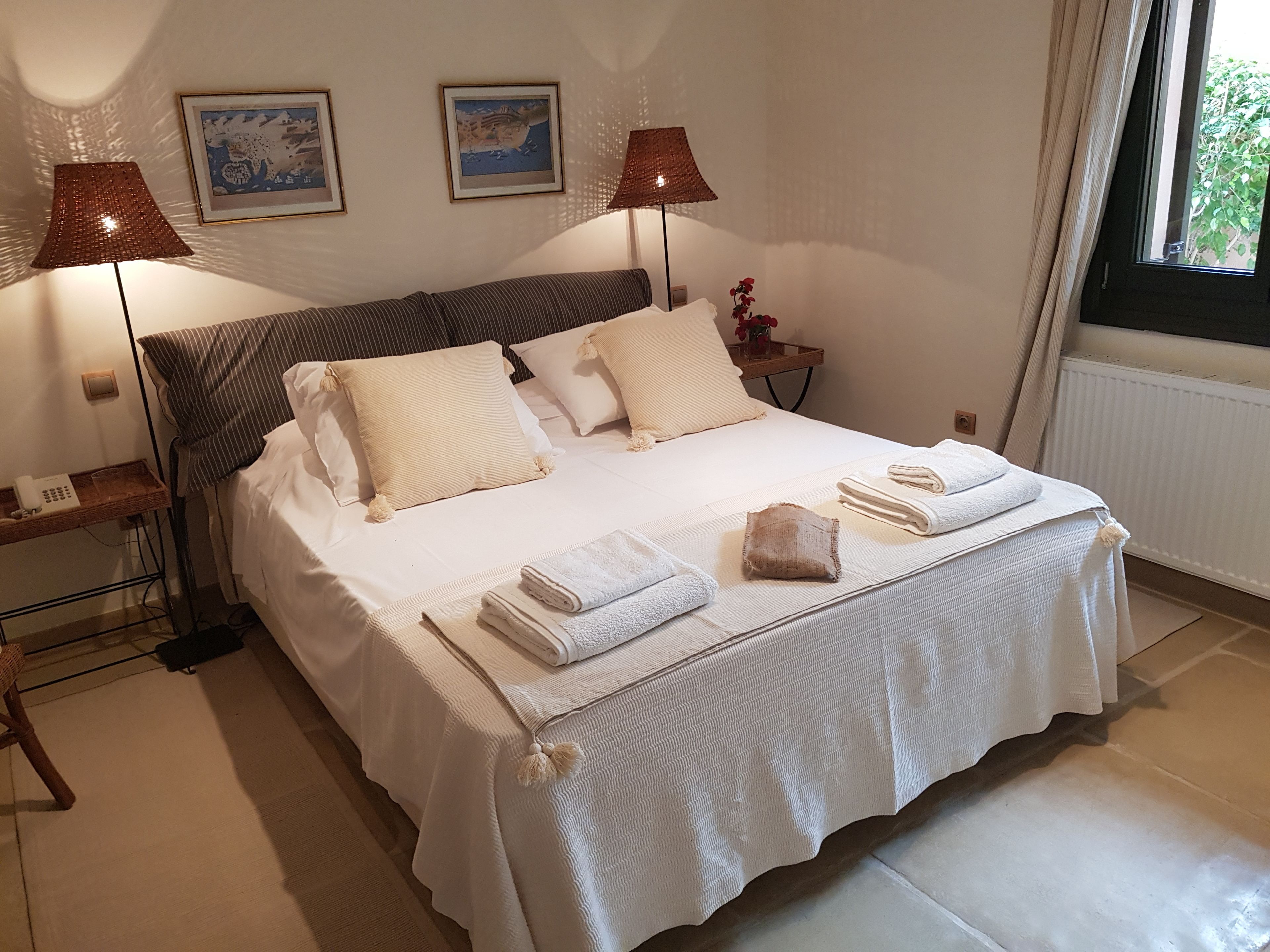 A neatly made bed with white linens and towels, two bedside lamps, and framed artwork on the wall.