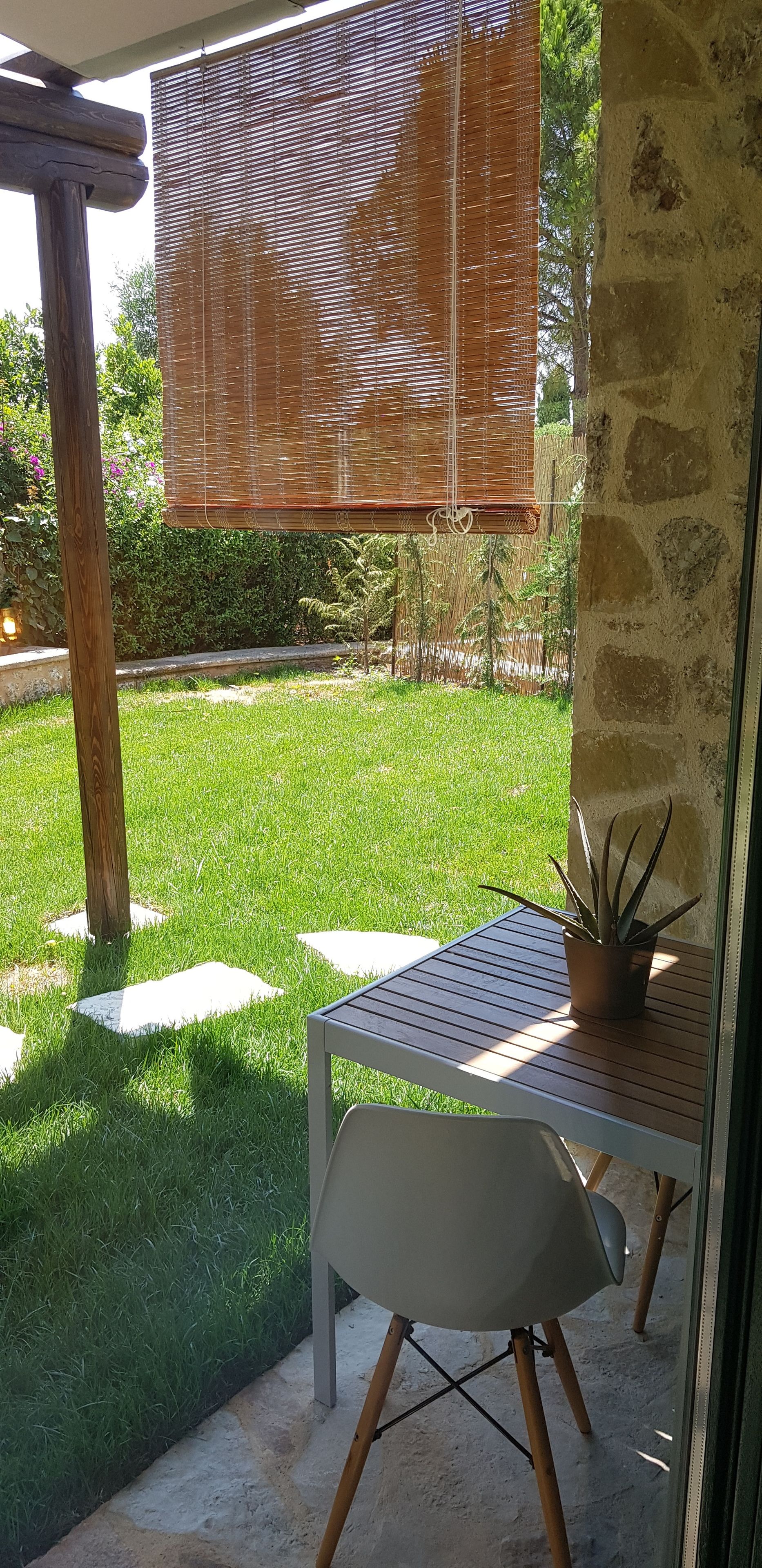 A patio area with a table and chair, a wooden pergola, and a view of a well-maintained lawn and garden.