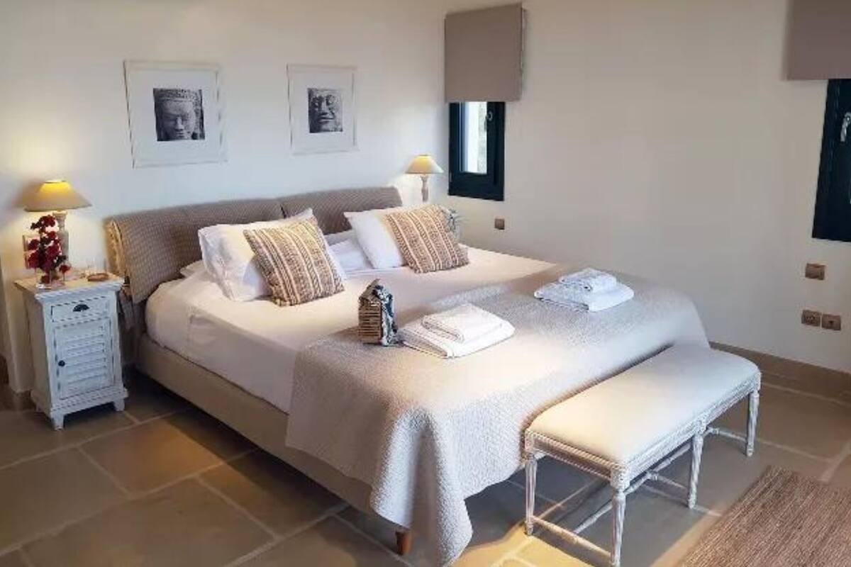 A neatly arranged bedroom with a large bed, two bedside tables, a bench, and two wall-mounted lamps.