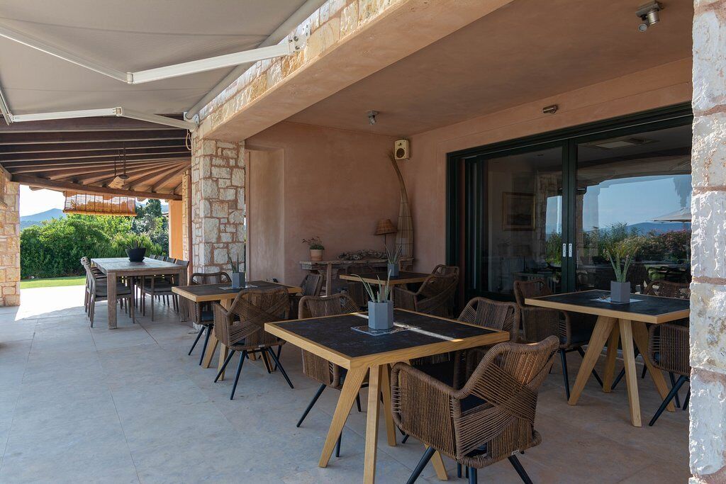 An outdoor patio area with multiple tables and wicker chairs, stone walls, and a glass door leading to a garden.