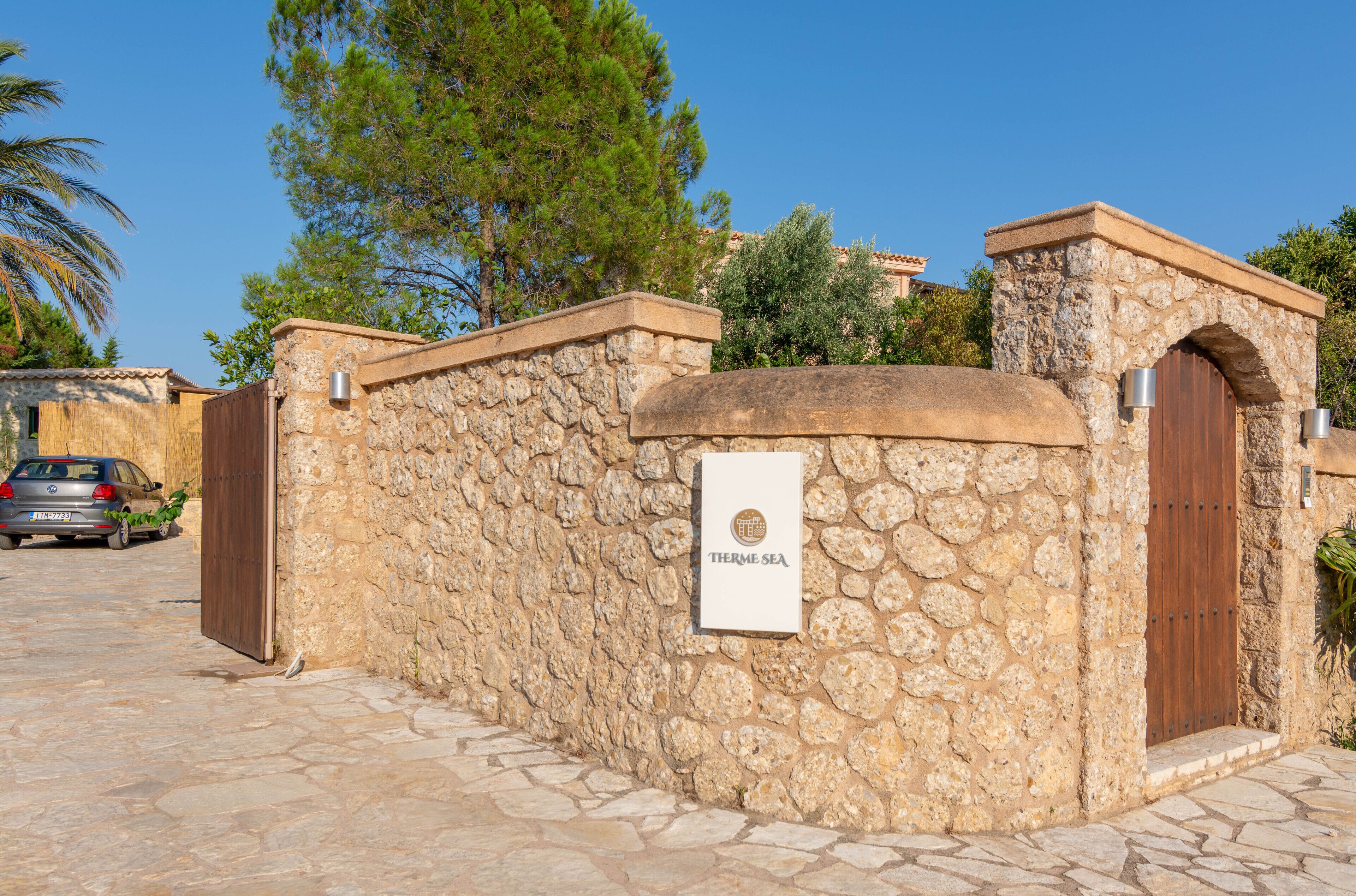 A stone wall with a sign reading "Therme Sea," a wooden door, and a parked car.