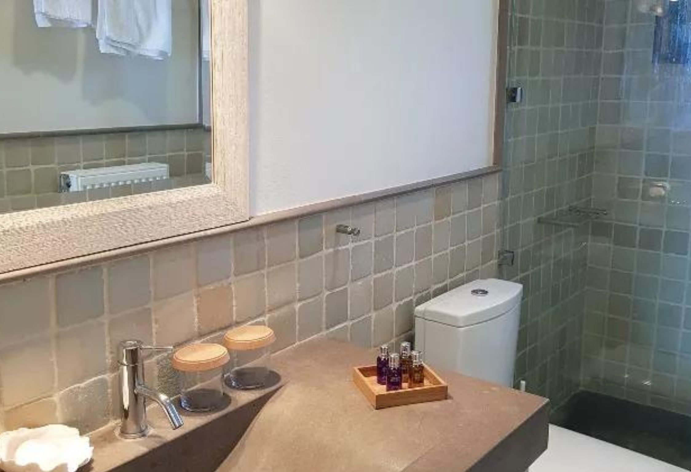 Un baño con un espejo grande, un lavamanos con artículos de tocador y una zona de ducha.