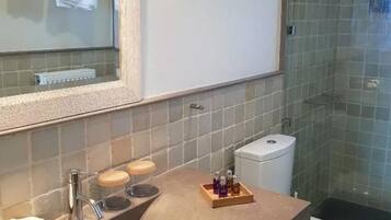 Un baño con un espejo grande, un lavamanos con artículos de tocador y una zona de ducha.