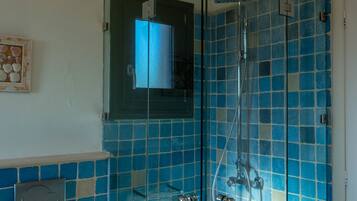 A glass-enclosed shower with blue tiles, a wooden toilet, and a small shelf with a decorative item.