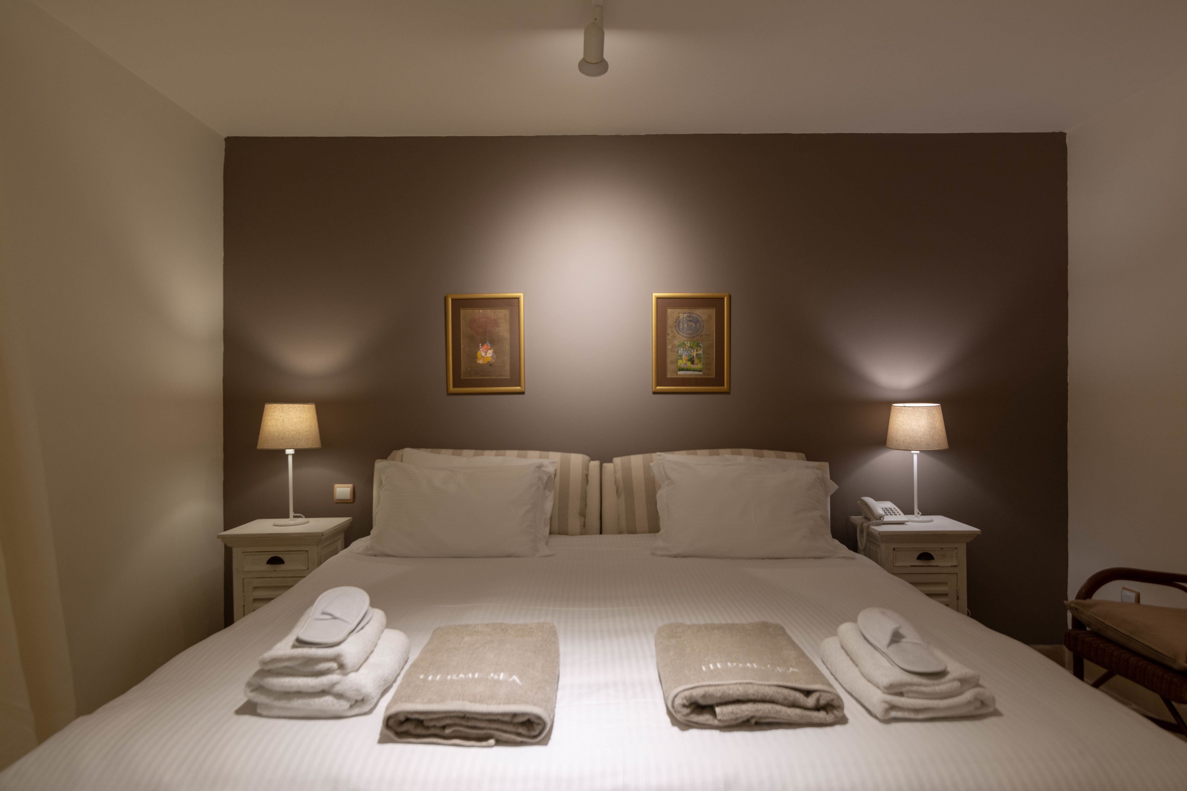 Habitación de hotel con una cama grande, dos mesitas de noche con lámparas y un cabecero con dos cuadros enmarcados.