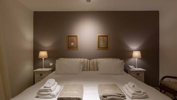 Habitación de hotel con una cama grande, dos mesitas de noche con lámparas y un cabecero con dos cuadros enmarcados.