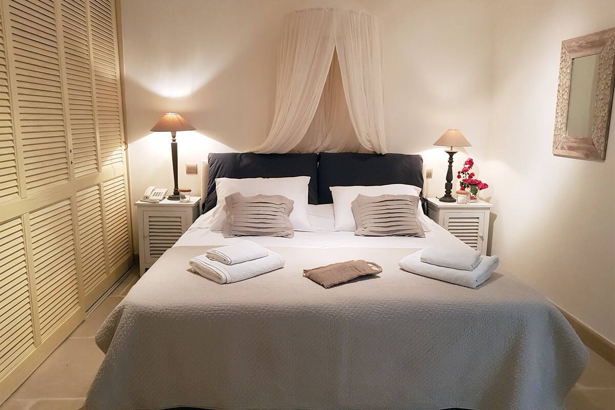 A neatly made bed with white linens and pillows, a canopy, and two bedside tables with lamps and a phone.