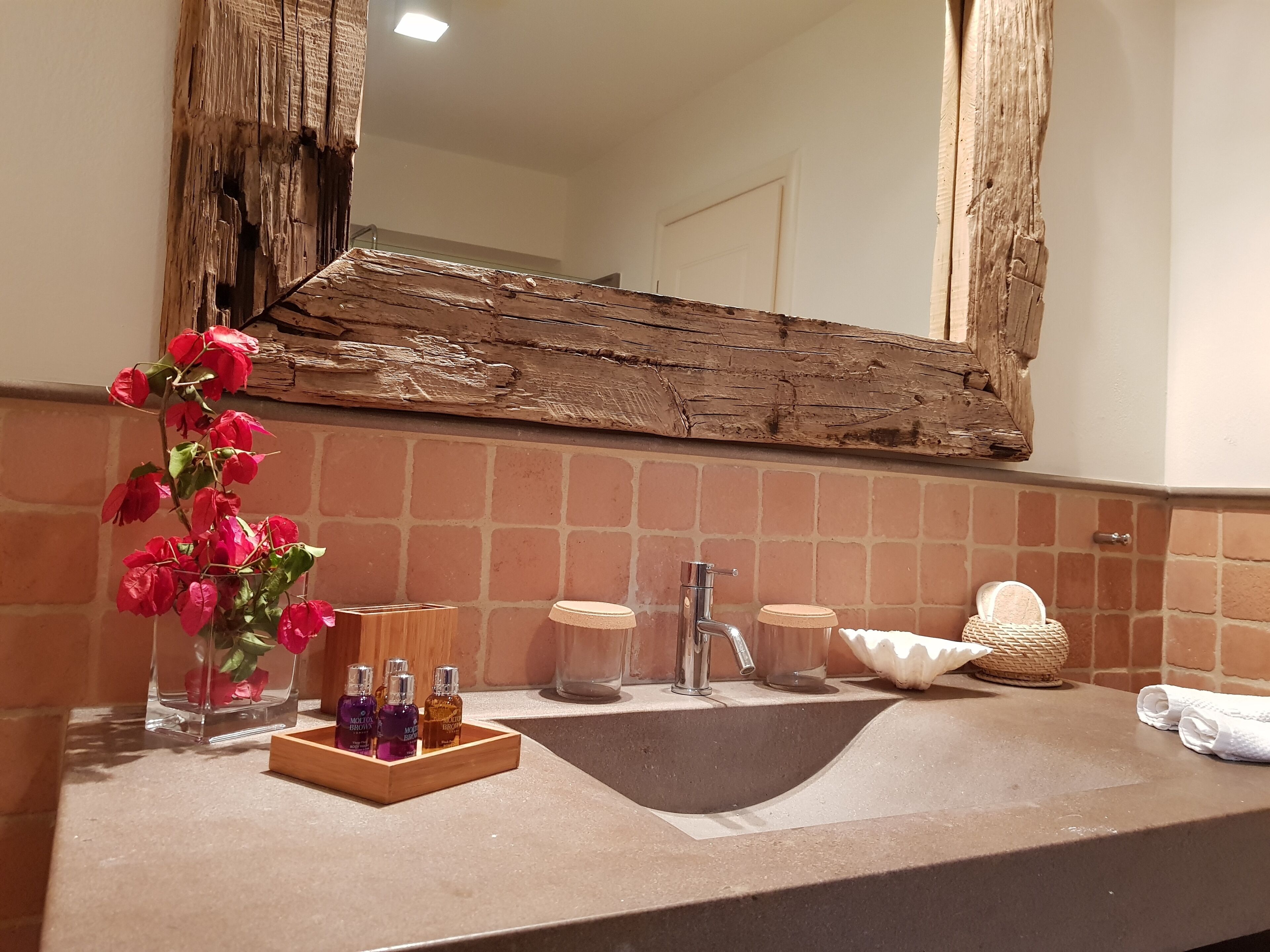 A bathroom with a large mirror, a sink, and a vase of red flowers.
