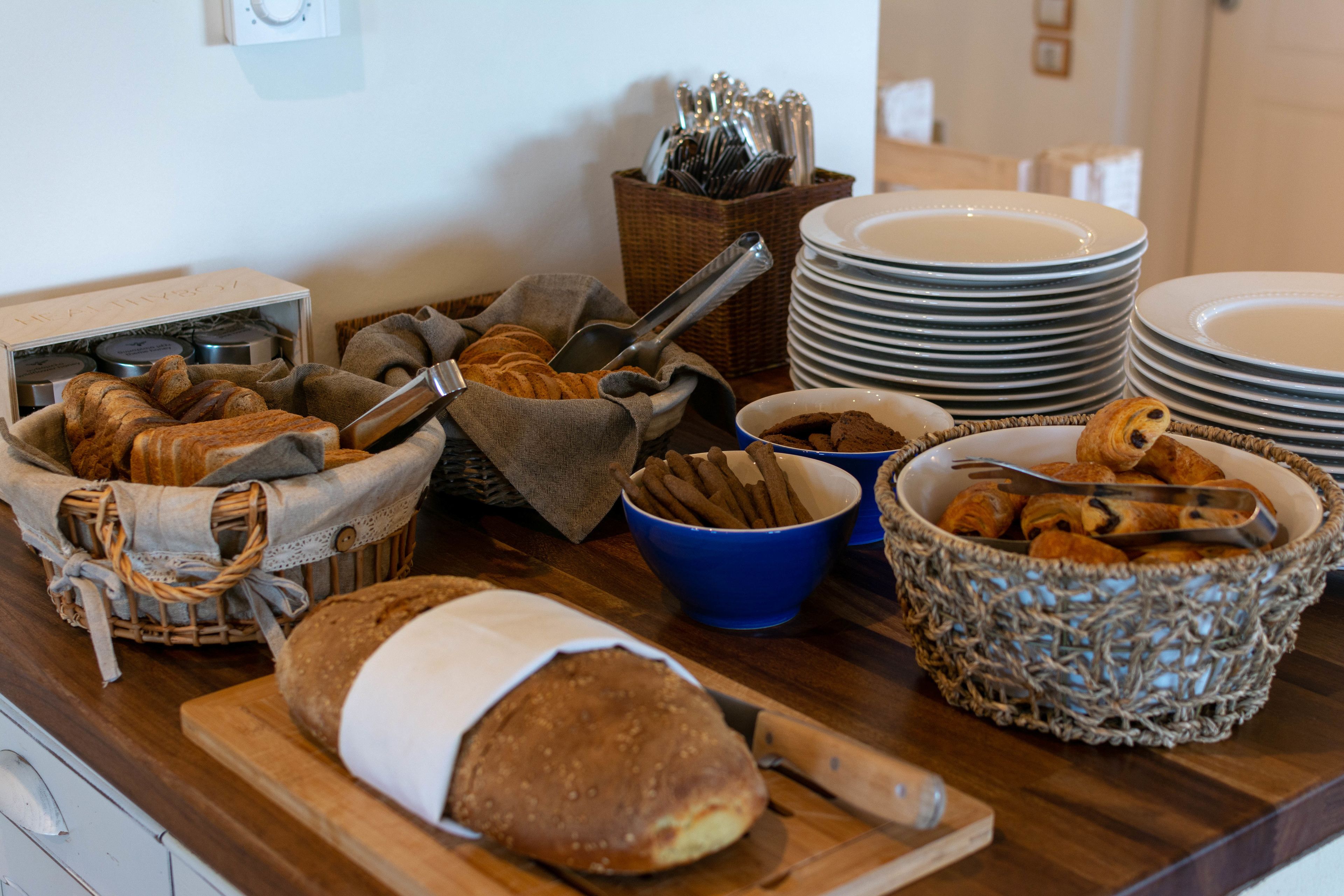 A breakfast buffet with various breads, pastries, and utensils.