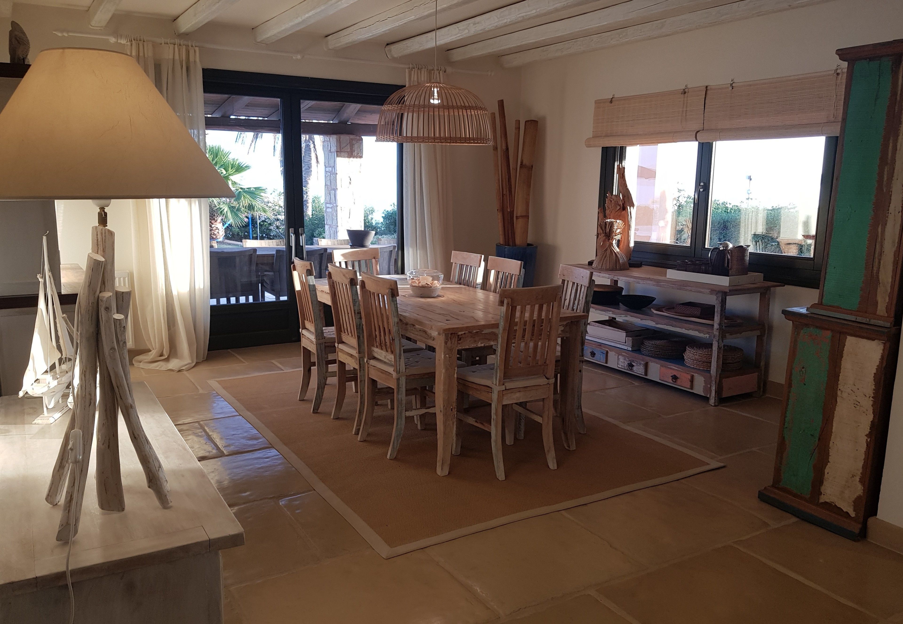 Un área de comedor con una mesa y sillas de madera, una lámpara colgante y vistas al exterior a través de amplios ventanales.