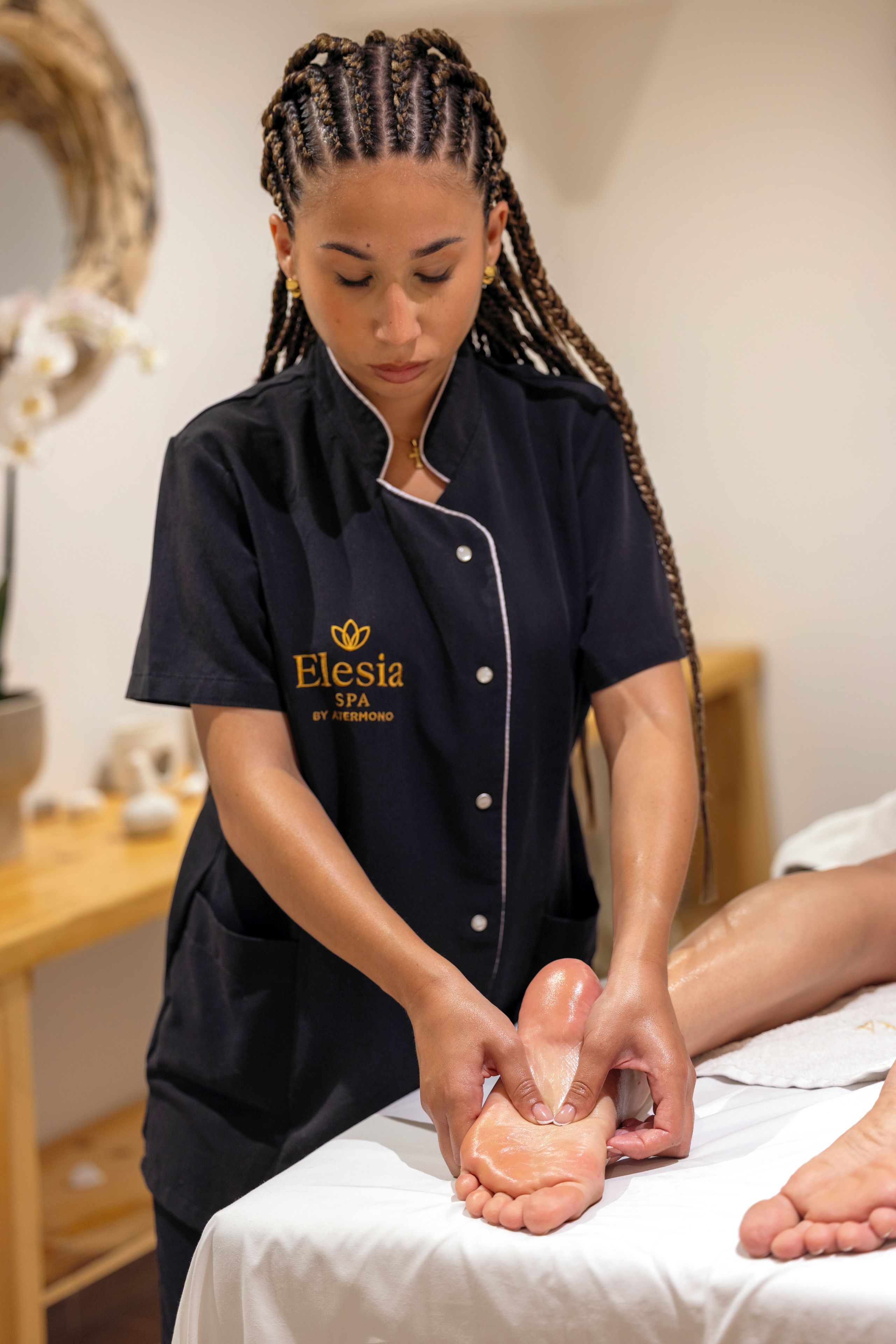 A person in a black uniform with 'Elesia SPA by Aiernondo' text, performing a foot massage on a client.