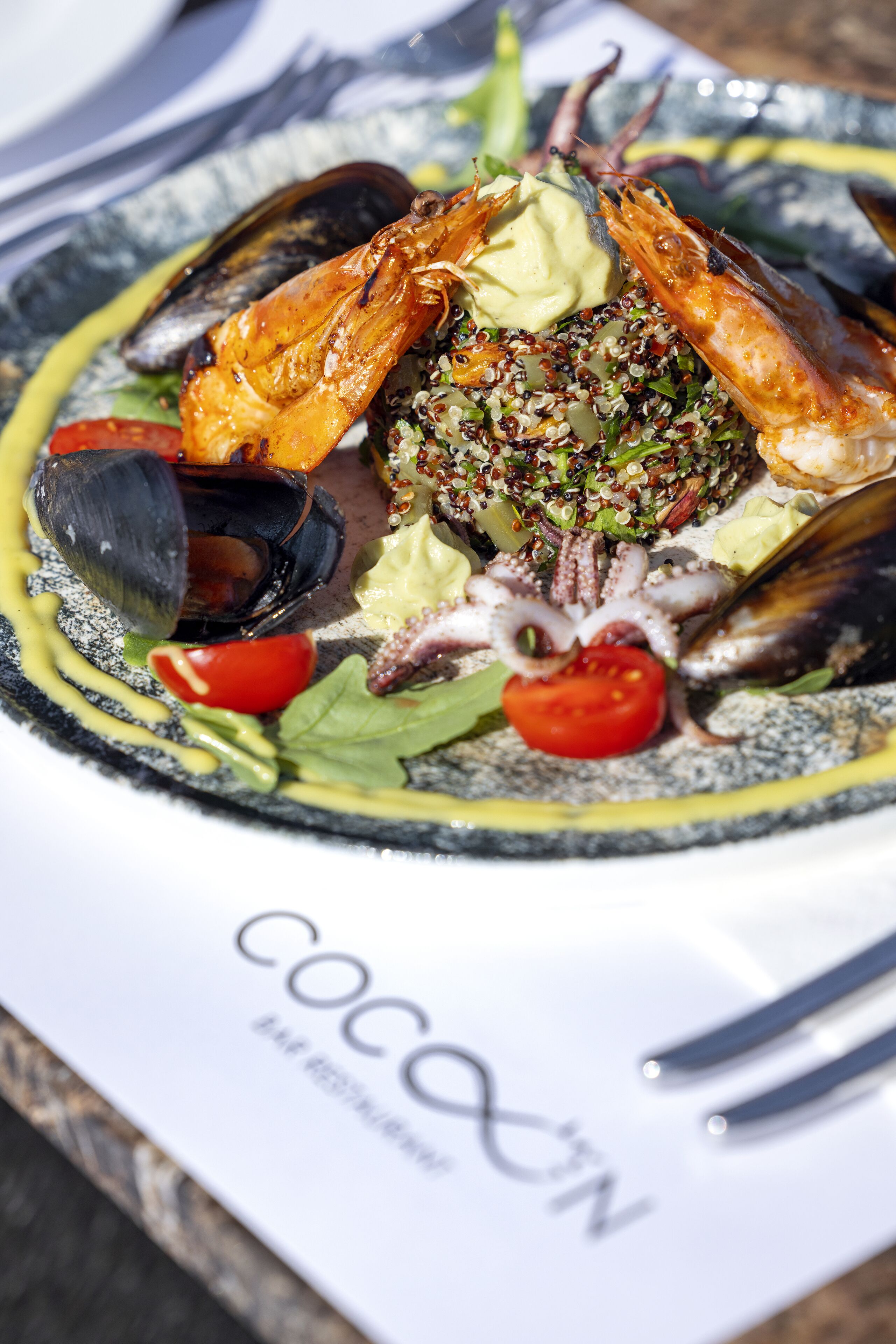 Un plat de fruits de mer présenté dans une assiette, accompagné d’une étiquette portant l’inscription « COCOON ».