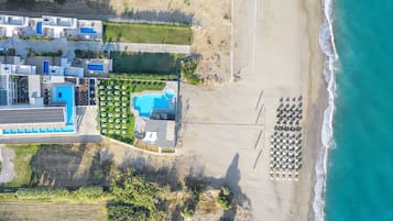 Vista aérea de un hotel costero con múltiples piscinas, una playa con sombrillas y un estacionamiento.