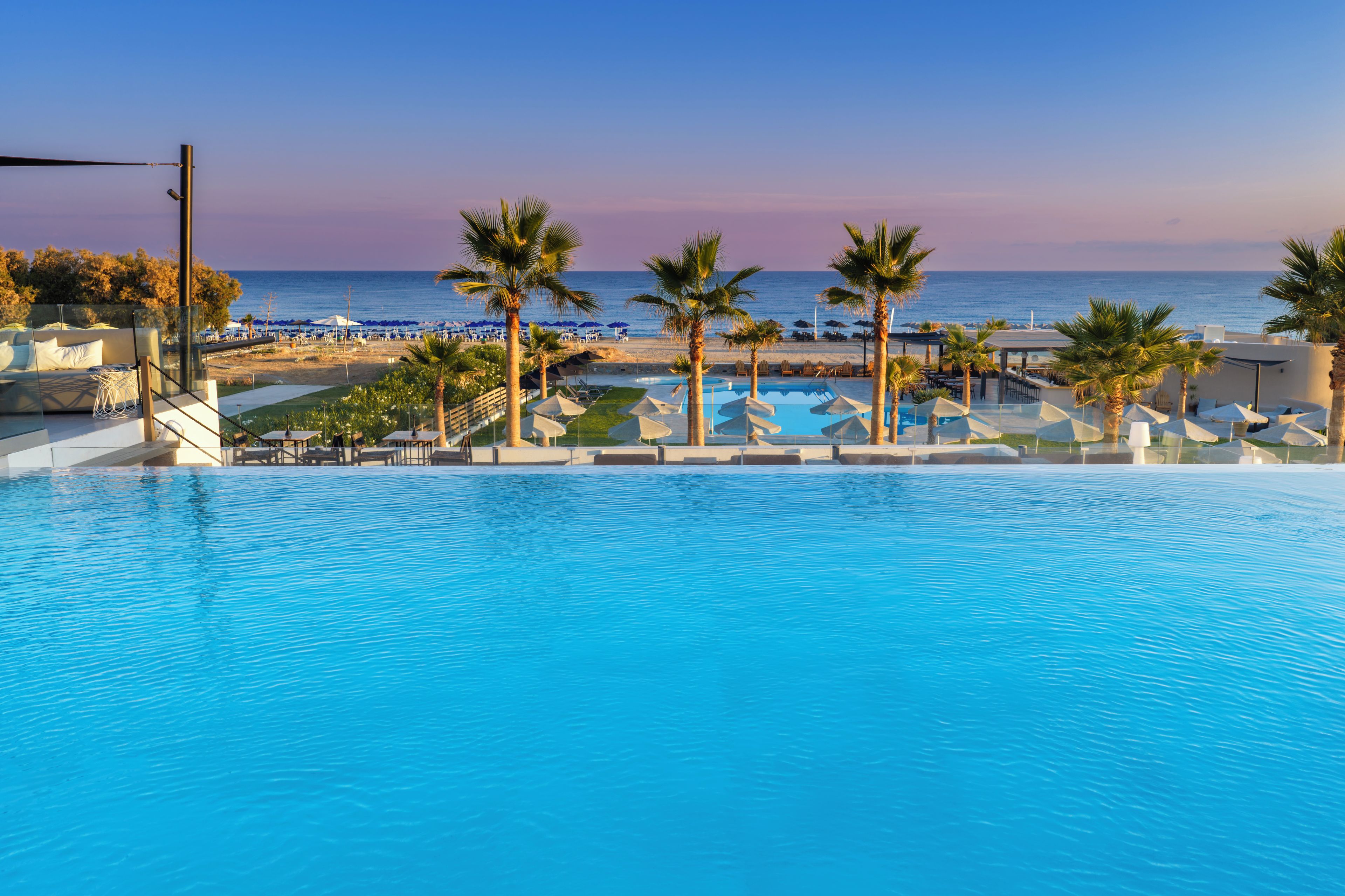 A pool area with lounge chairs and umbrellas, overlooking a beach and the ocean.