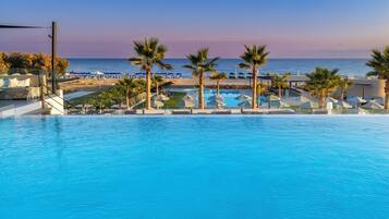 A pool area with lounge chairs and umbrellas, overlooking a beach and the ocean.