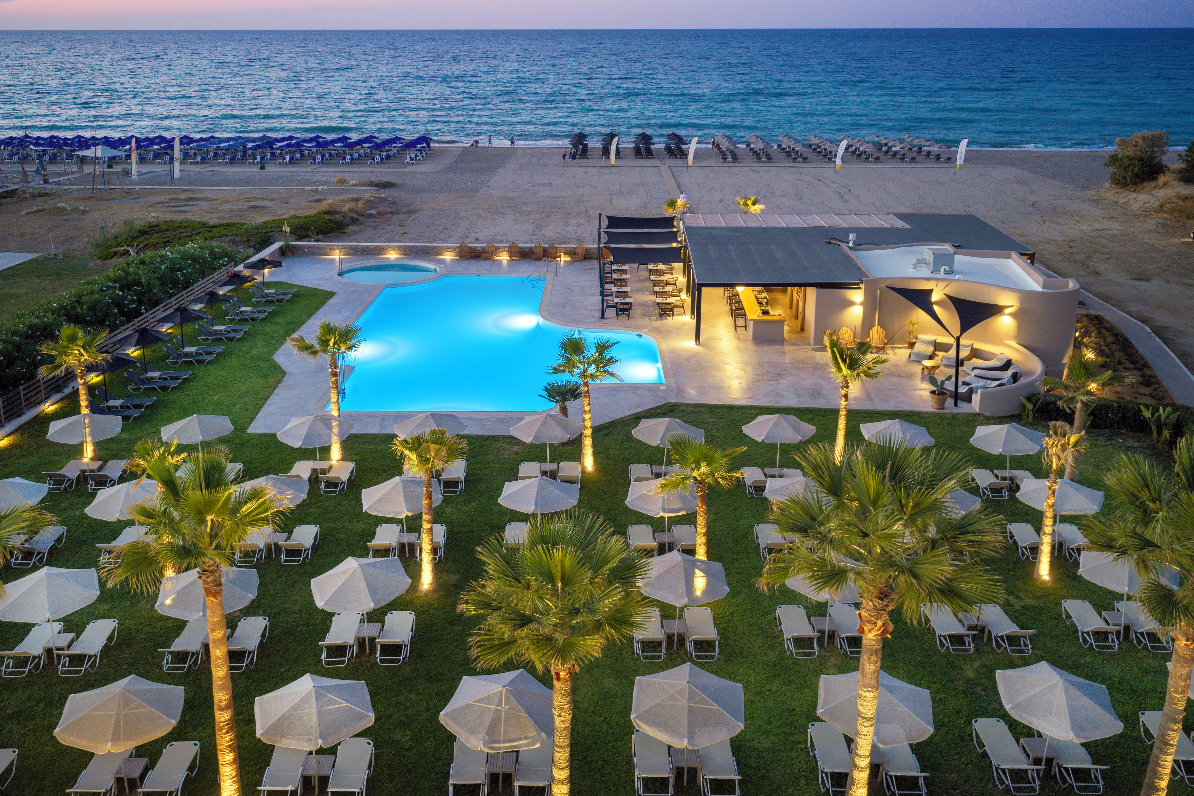 A resort with a swimming pool, beach chairs, umbrellas, and a dining area.