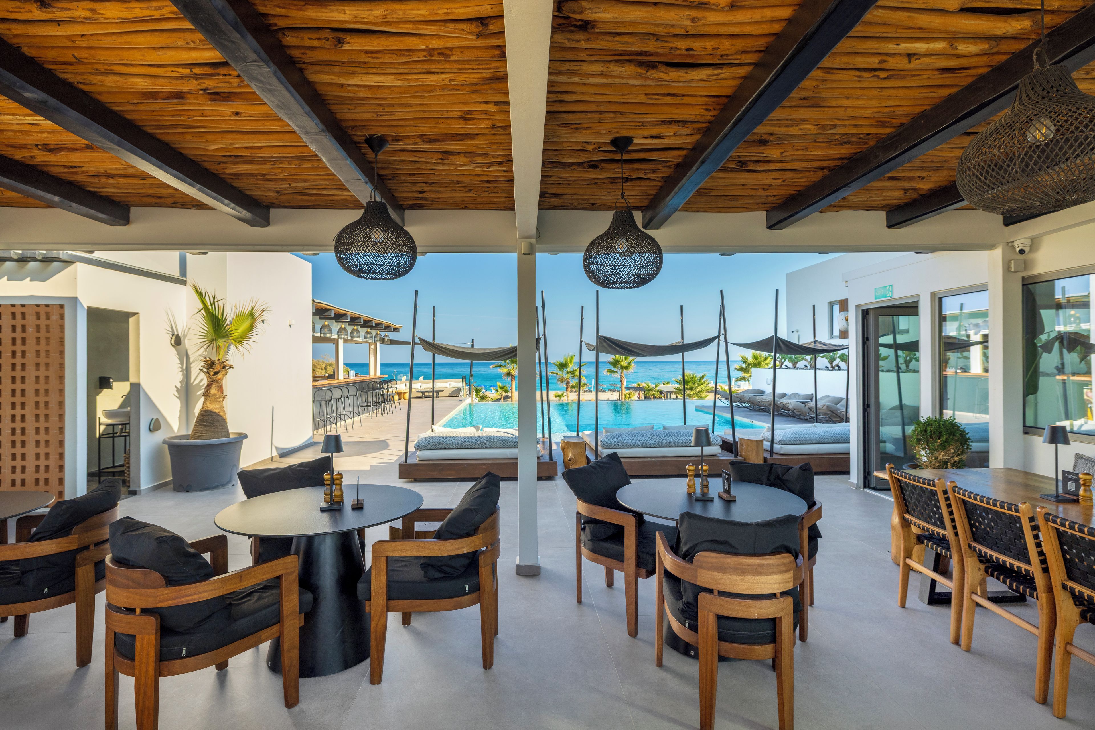 Ein Außenbereich mit Tischen und Stühlen mit Blick auf einen Pool und das Meer.