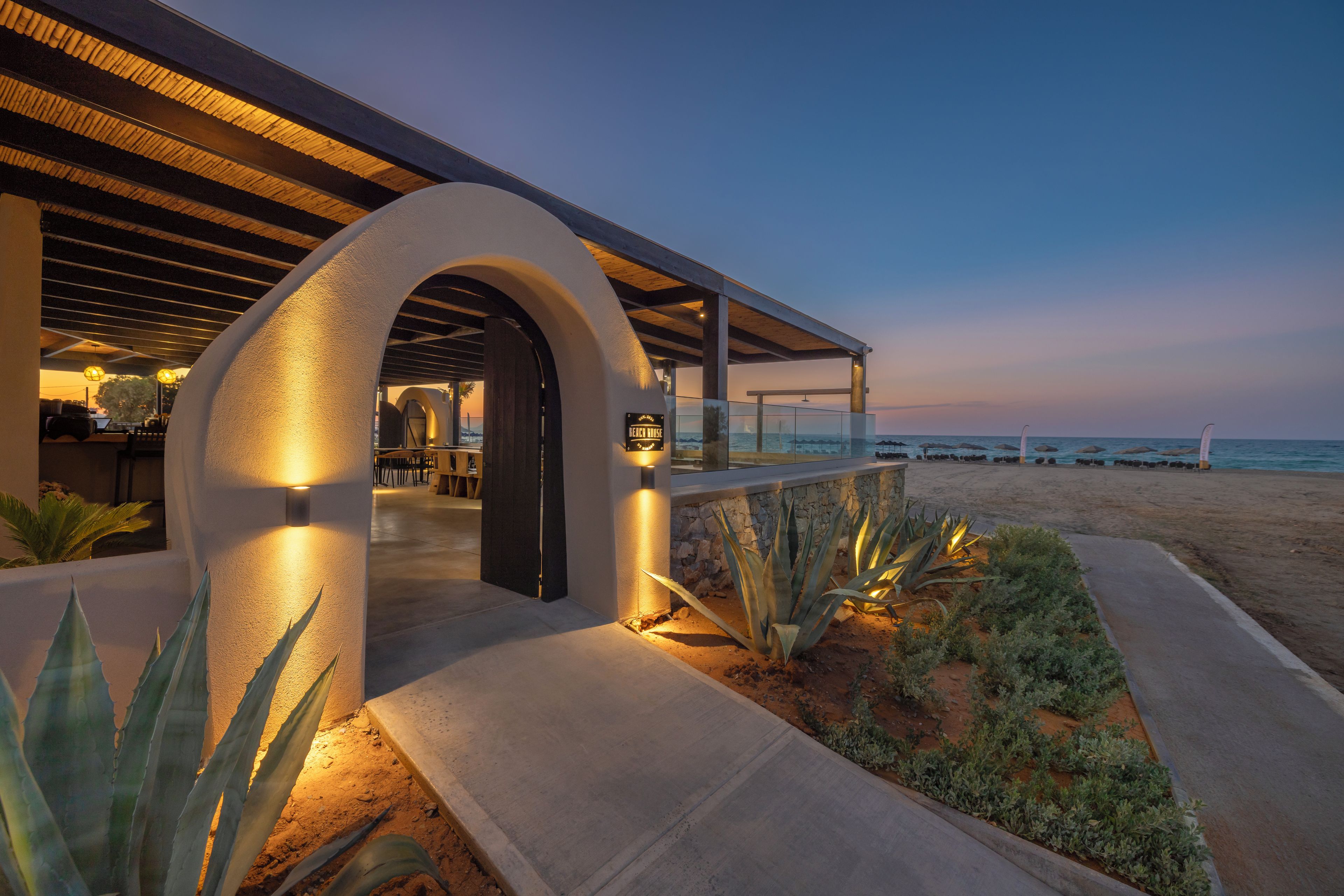 A beachfront property with a covered patio, a sign indicating 'Beach House', and a view of the ocean.