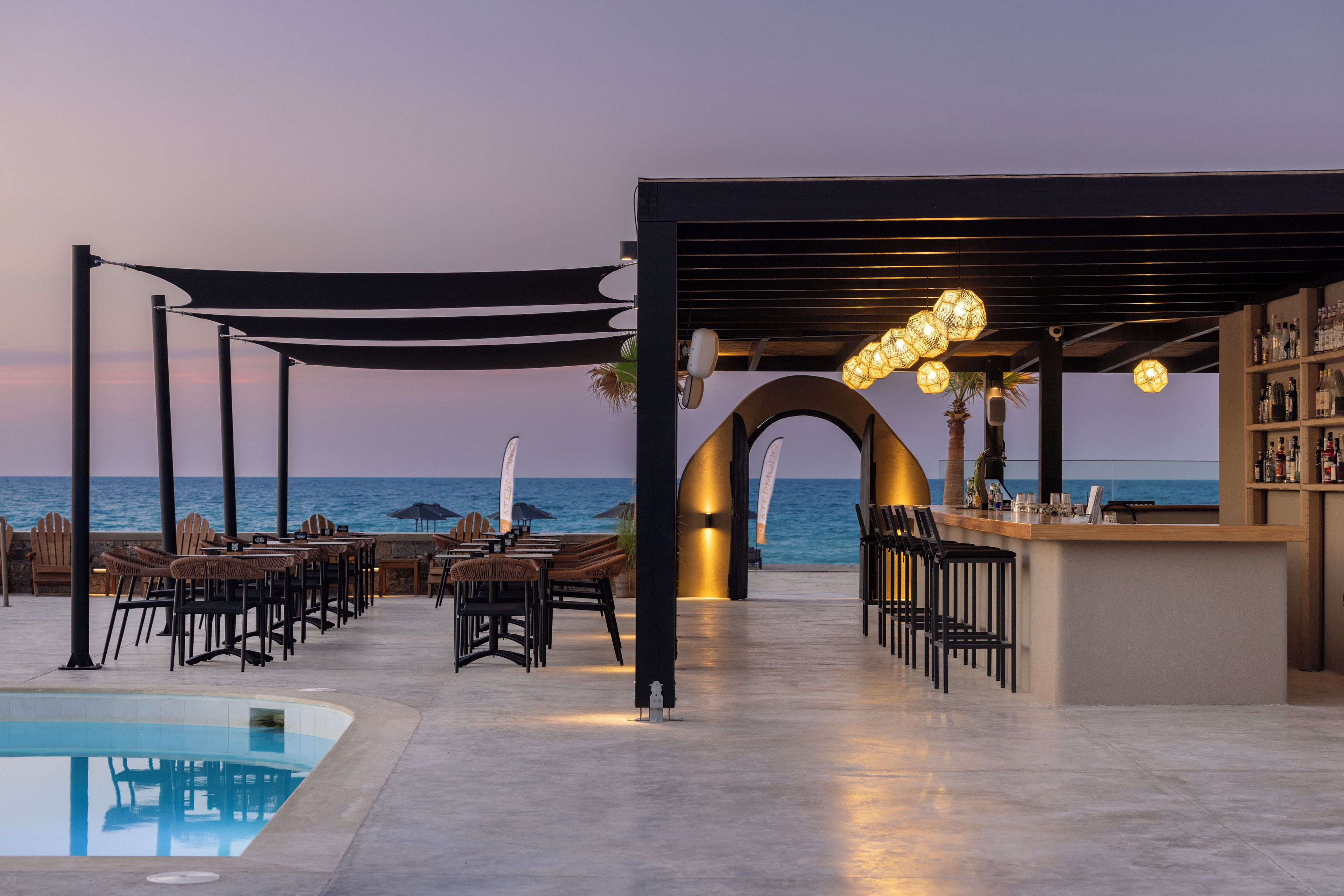 A poolside bar area with outdoor seating and a view of the sea.