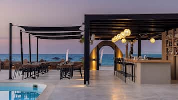 A poolside bar area with outdoor seating and a view of the sea.